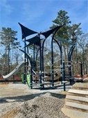 Newly installed playground equipment in a open field with pine forest behind it