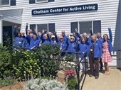 A group of older adults wearing blue fleece jackets with their hands raised in the air