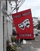 Red First Night banner with two white drama masks hangs from a flagpole on Main Street business