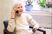 Senior woman sitting in a chair wearing a white sweater talking on the phone.