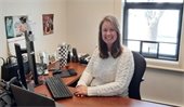 Candace Cook seated at a desk in front of a window smiling at the camera