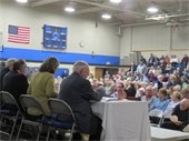 Members of the Select Board seated on the dais in front of Annual Town meeting audience