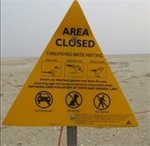 Yellow triangular sign and orange roping on a beach