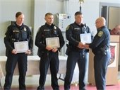 Three police officers holding certificates the last in line shaking hands with another officer