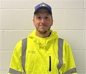 Young man in blue ball cap and Hi Vis gear standing against a white cinderblock wall