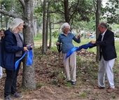 Barbara Cotnam smiling broadly after cutting a blue ribbon with oversized scissors