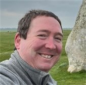 Doug Berman outside in a grassy field with a large rock to his left