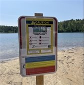Caution sign mounted on a beach by a pond in the woods