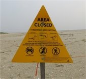 Yellow triangular sign and orange roping on a beach