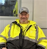 Man in high visibility gear wearing a gray ball cap seated and smiling
