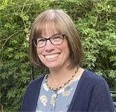 A woman with shoulder length brown hair wearing dark rimmed glasses smiling at the camera