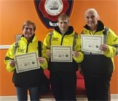Three women in Hi Vis jackets holding certificates in front of an orange wall