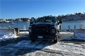 Dark blue pick-up truck parked on a bulkhead beside water between concrete barriers