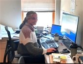 Woman seated at a desk in front of a computer screen smiling.