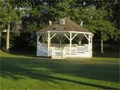 white bandstand in a park surrounded by green grass and trees