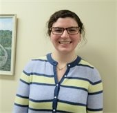Woman with dark hair pulled back and glasses wearing a blue and yellow striped sweater smiling