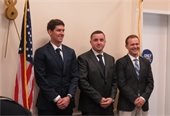 Three young men in suit jackets and ties standing next to an American flag