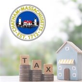 Three stacks of coins with Scrabble tiles on each spelling "tax" next to a model house