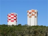 Two water tower tanks painted red and white with tree line in the foreground
