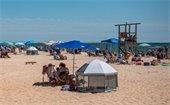 People sitting in chairs under umbrellas around a lifeguard stand on a beach