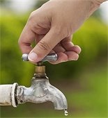 Hand turning off a dripping outdoor spigot