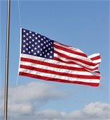 American flag flying at half-staff against blue sky