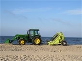 Green tractor towing a yellow trailer on a beach
