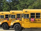Three yellow school busses lined up in a lot.