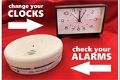 Alarm clock and a smoke detector on a red background with text reading Change your clock, check your alarms