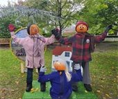 Three figures dressed in winter clothes with pumpkins as heads outdoors in a park.