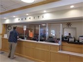 Person standing at a counter with the word PERMITS spelled out on the wall above