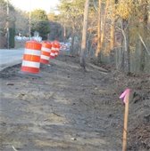 Orange and white construction barrels along a road where the shoulder has been cleared of vegetation