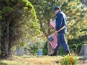 Coast Guardsman in dark blue uniform placing flags in a cemetery.