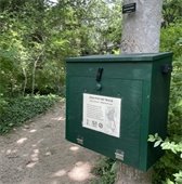 Green wooden box on a tree along side a path in the woods