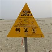 Yellow triangular sign and orange roping on a beach