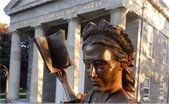 Statue of Mercy Otis Warren holding book in outstretched hand in front of Columned stone building