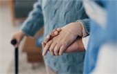 Close up of a hand holding the hand of an older person walking with a cane