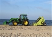 Green tractor pulling a beach rake on a sandy beach